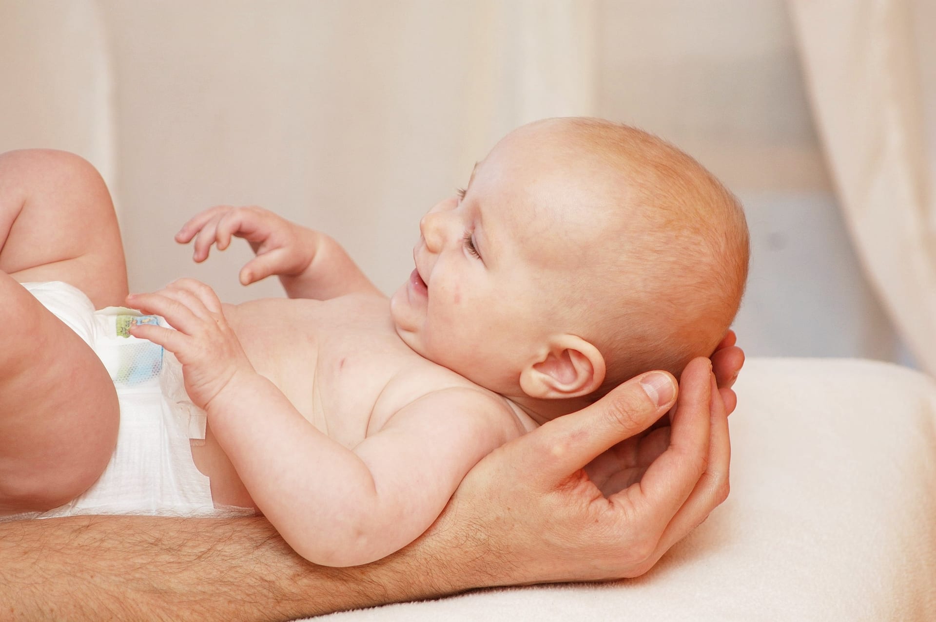 Baby resting along a practitioner's forearm while a hand gently cradles the back of its head